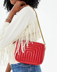 Woman carrying a Clare V Midi Sac in Rouge Channel Quilted Nappa with a red fringed crossbody strap.