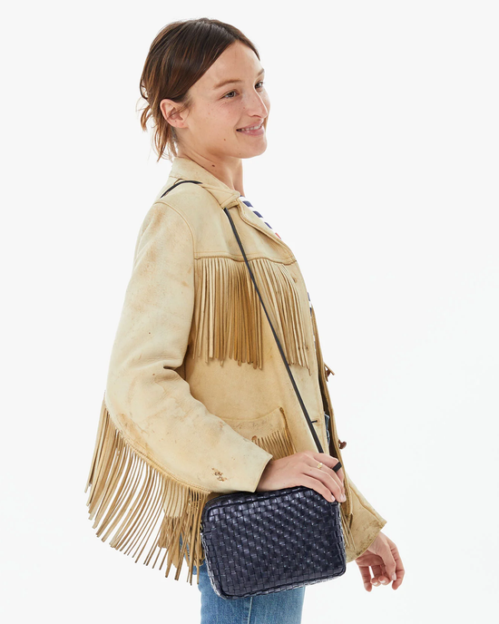 Woman smiling in profile view, wearing a fringed light jacket and carrying a Clare V Midi Sac in Twilight Woven Checker crossbody bag.