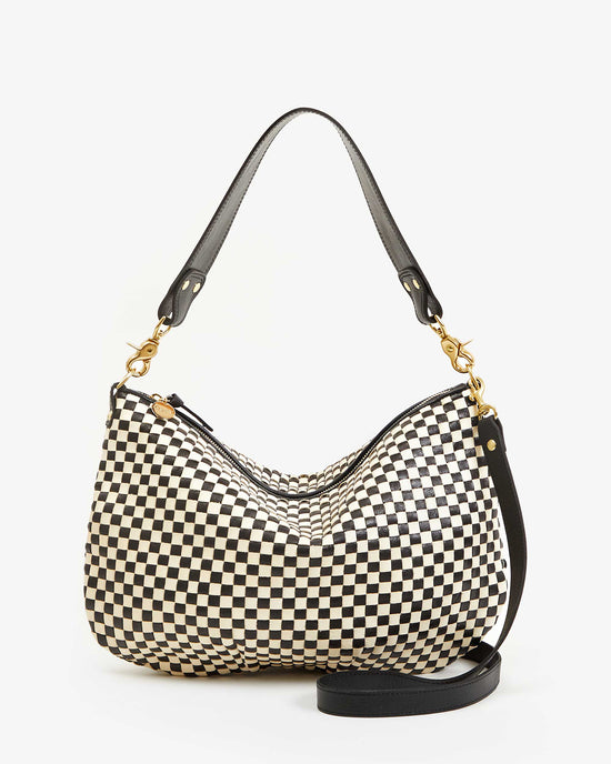 The Clare V. Woven Checker Moyen Messenger in Black & Cream is a medium-sized leather bag with a black and cream checkered design, gold hardware, short black top handle, detachable strap, and is handmade in Bangladesh.
