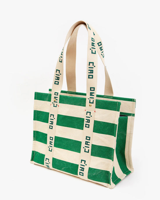 Noemie in Palm Green & Natural Canvas Stripe tote by Clare V. with "ciao" printed repeatedly on the straps, isolated on a white background.