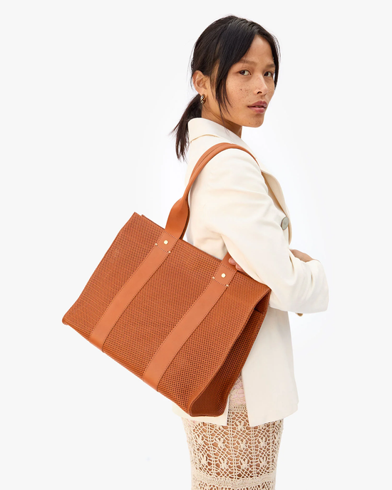 Woman in a white blazer carrying a large brown Clare V. Noemie in Cuoio Perf tote bag on her shoulder.