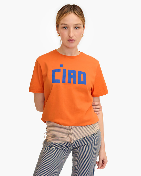 Young woman in a Block Ciao Original Tee in Zucca w/ Cobalt by Clare V., paired with striped pants, standing against a white background.