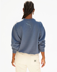 Back view of a person wearing a blue Clare V. Oui Oversized Sweatshirt in Faded Navy w/ Light Blue with an oversized fit and white pants.