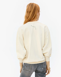 Woman from behind wearing a Clare V. Grand Block Ciao Oversized Sweatshirt in Cream / Evergreen made of 100% cotton fleece and gray jeans.