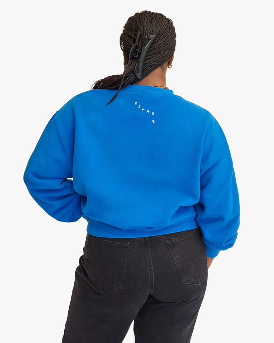 Back view of a person wearing a Clare V. Block Ciao Oversized Sweatshirt in Bright Cobalt w/ Cream, and black jeans, with braided hair gathered in a clip.