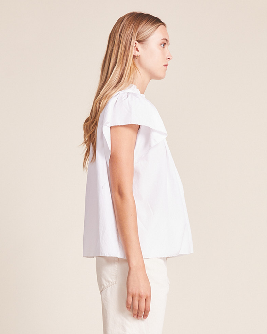 Profile view of a woman in a Trovata Birds of Paradis Carla Highneck Shirt in White with ruffle sleeves and light-colored pants.