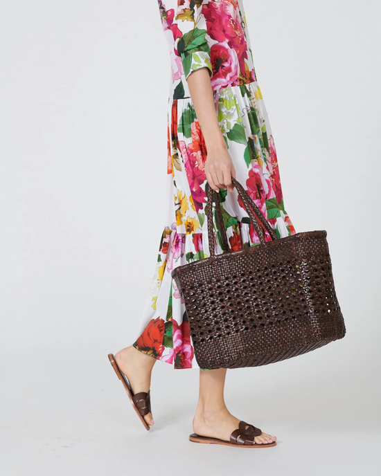 A person in a floral dress carrying a Dragon Diffusion Cannage Max in Dark Brown handwoven leather tote and wearing brown sandals.
