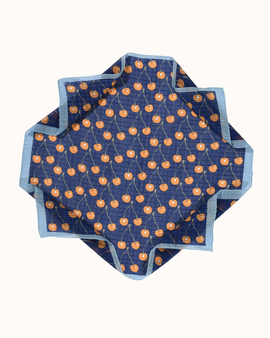 An octagonal Botanica Cherries Bandana in Ultramarine tablecloth with an orange fruit pattern on a white background, featuring a lightweight weave by Épice.
