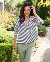 Woman smiling and walking in a garden, wearing a Patrick Popover Henley in White & British Royal Navy by Frank & Eileen and green pants.