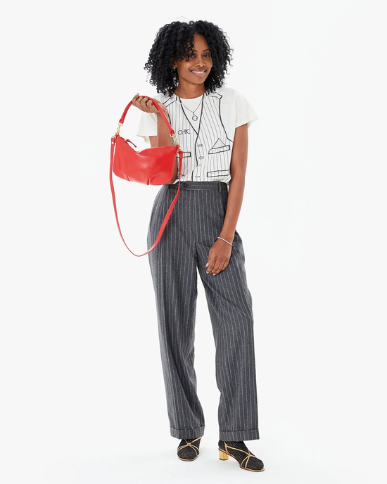 Woman posing with a Clare V. Petit Moyen Messenger in Rouge Nappa Luxe handbag, wearing striped trousers and a white t-shirt.