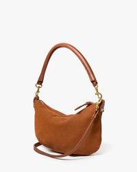 The Clare V. Petit Moyen Messenger in smooth hazelnut nubuck features a curved handle, detachable strap, and gold-tone hardware—a chic crossbody bag set against a plain white background.