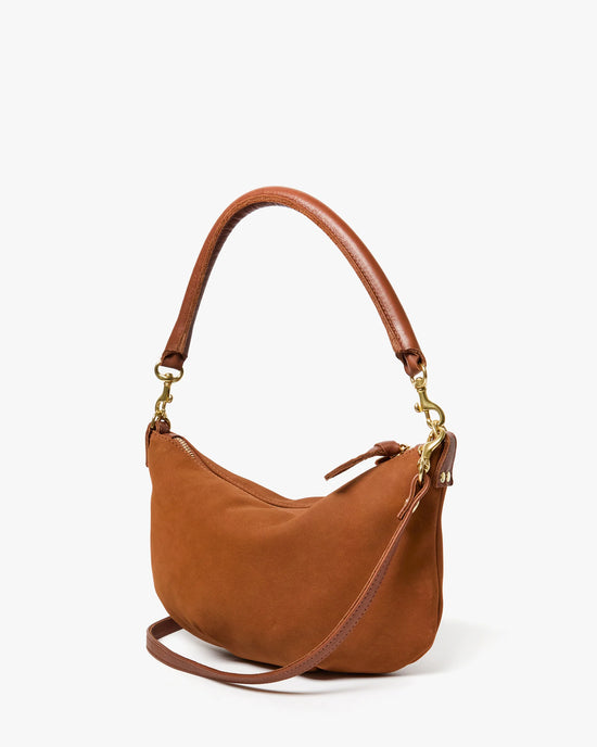 The Clare V. Petit Moyen Messenger in smooth hazelnut nubuck features a curved handle, detachable strap, and gold-tone hardware—a chic crossbody bag set against a plain white background.