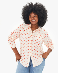 Woman smiling and posing in a Clare V. Phoebe Blouse in Blush w/ Poppy Allover Lips with a red heart pattern and blue jeans.