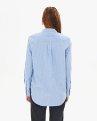 A person standing with their back to the camera, wearing a Clare V. Phoebe Blouse in Blue & Cream Stripe and black trousers.