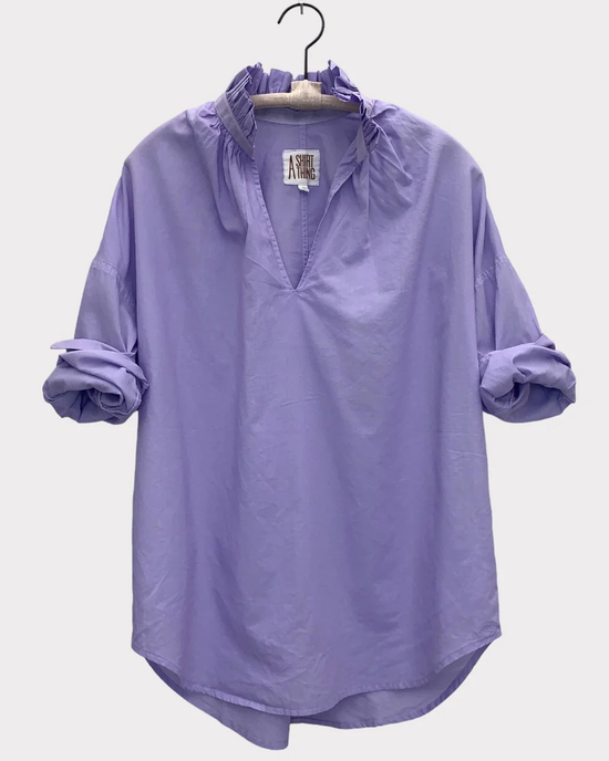A Penelope - Cabo in Lilac pop over shirt with ruffle collar and gathered sleeves, displayed on a hanger against a white background by A Shirt Thing.