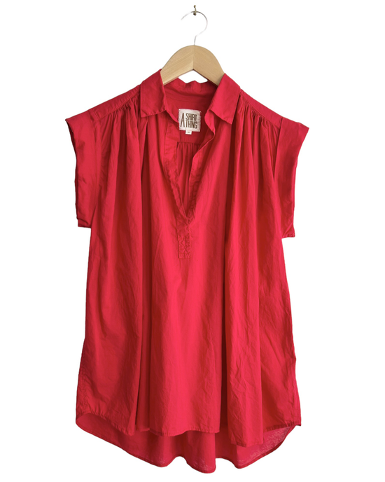 Sleeveless V-neck blouse in Liv - Cabo in Poppy by A Shirt Thing, with shirring along the shoulder, hanging on a wooden hanger against a white background.