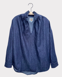 A Penelope - Denim in Indigo shirt with a ruffle collar hanging on a white hanger, displayed against a plain background by A Shirt Thing.