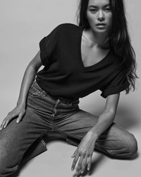 A monochrome portrait of a woman in a casual pose wearing a Nation LTD Stevie Cuffed V Neck in Jet Black t-shirt and jeans.