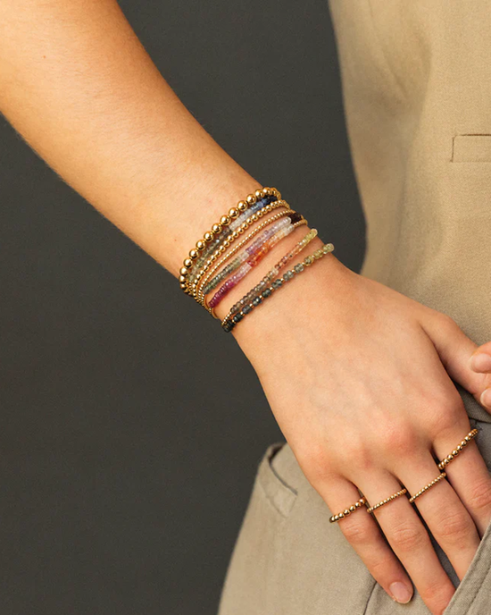 A person's wrist adorned with multiple Karen Lazar Design 2MM Sig Bracelets with Vino Ombre & Yellow Gold, featuring 14k Yellow Gold filled beads and Sapphire gemstones.