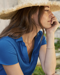 A woman in a Frank & Eileen Lauren S/S Polo Jersey Dress in Summer Blue appears contemplative as she rests her chin on her hand.