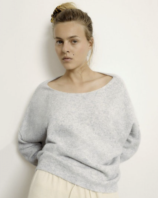 Woman in an American Vintage Damsville Boatneck Sweater in Gris Chine and beige skirt with a hair clip in her pulled-back hair, posing against a white background.