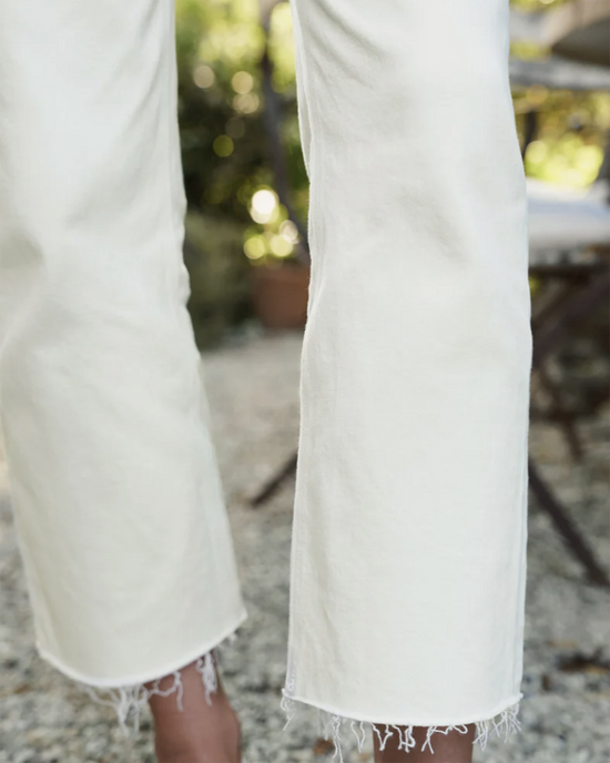 A close-up of white Frank & Eileen Monaghan Mom Jean pants with frayed hems and a partial view of a person's leg in an outdoor setting.