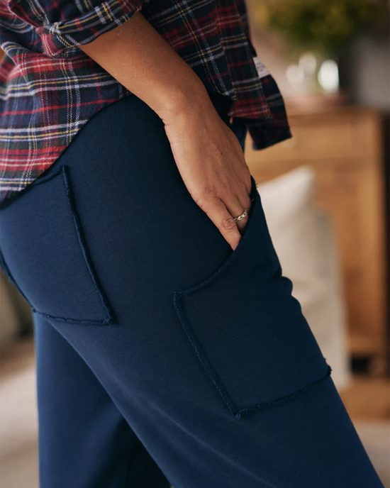A person standing with their hand resting on their hip, wearing a plaid Triple Fleece shirt and blue Eamon Jogger sweatpants in Air Force with roomy patch pockets by Frank & Eileen.