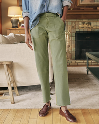 A person wearing Frank & Eileen's Blackrock Utility Pant in Army and brown loafers standing in a cozy room with a fireplace in the background.