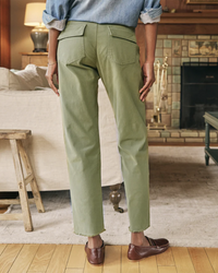 A person wearing Frank & Eileen's Blackrock Utility Pant in Army and brown leather shoes stands in a room with a fireplace in the background.