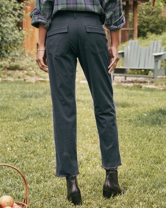 Person standing in a garden wearing dark Frank & Eileen Blackrock Utility Pants in Washed Black and a plaid shirt, with hands in pockets. A basket with apples is visible to the side.
