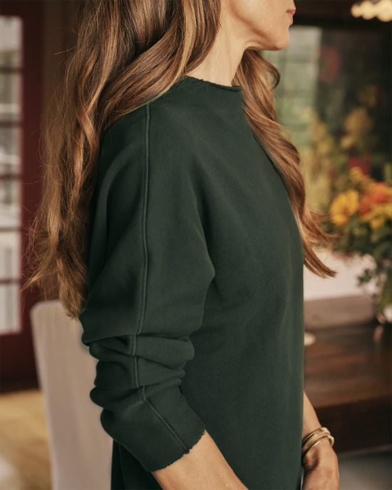 A person with long, wavy brown hair wearing a Izzie Funnel Neck Short Dress in Evergreen by Frank & Eileen, viewed from the side.