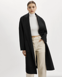 Woman posing in a white turtleneck, beige trousers, and a black Lamarque Thara Jacket with an oversized fit.