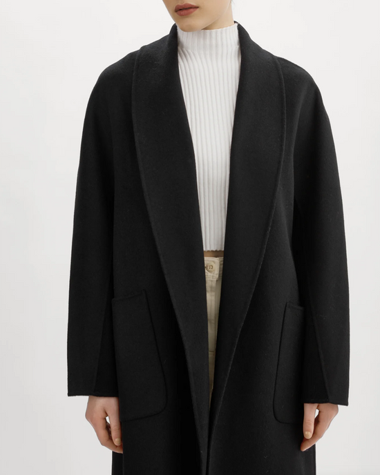 A person wearing an oversized Lamarque Thara Jacket in black, a white turtleneck, and beige trousers.