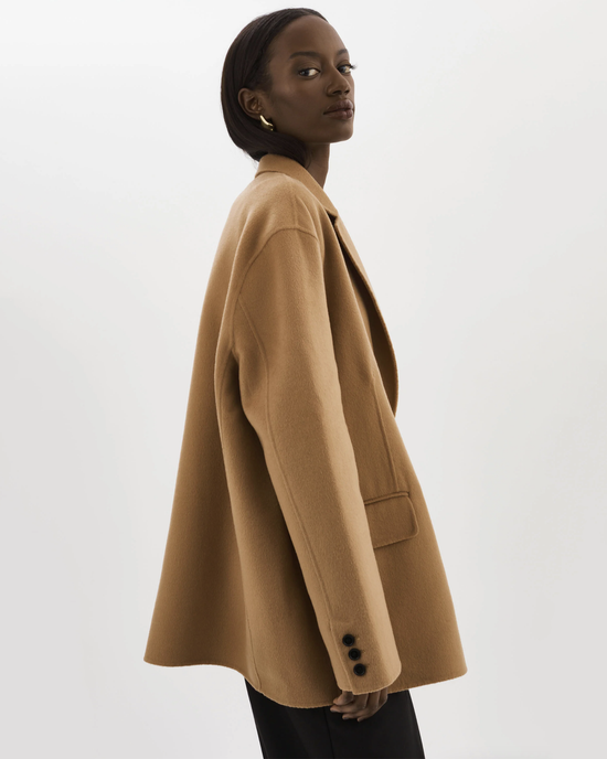 A woman in a tan oversized Ennis Jacket in Camel by Lamarque, looking over her shoulder with a neutral expression.