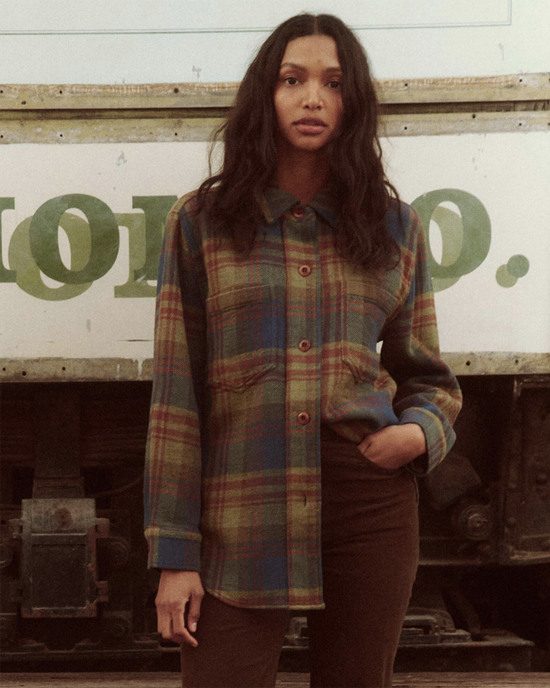 A woman in The Craftsman Jacket in Sequoia Plaid by the Great standing in front of a vintage industrial background.