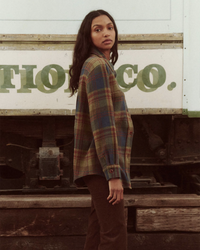 A woman in a The Craftsman Jacket in Sequoia Plaid by the Great standing in front of a rustic truck with the word "fiogco" visible on it.