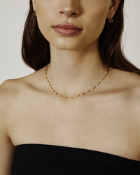 Woman wearing Chan Luu gold beaded necklace and earrings against a neutral background.