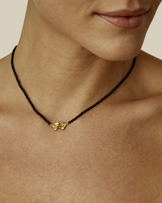 A close-up of a person wearing a Chan Luu Onyx Beaded Merida necklace with an 18k gold plated sterling silver pendant.