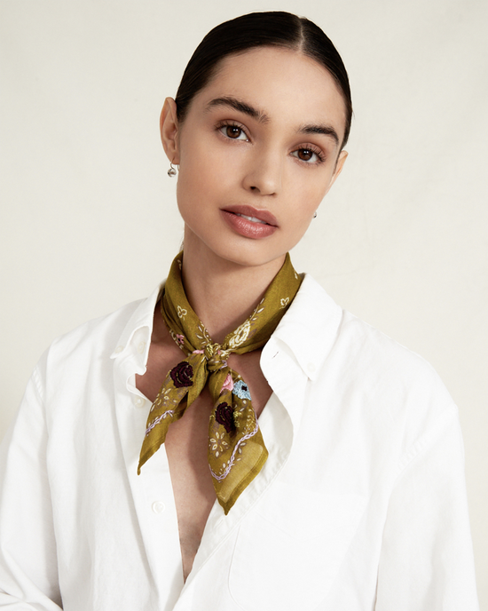 A woman in a white shirt wearing a Chan Luu Lrg Emb Flower Bandana in Green tied around her neck, with a focused, gentle expression.