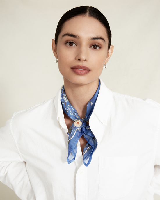 Portrait of a woman wearing a white shirt and a blue Chan Luu Lrg Emb Flower Bandana in Periwinkle tied around her neck, looking directly at the camera.