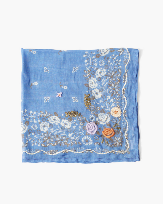Blue viscose gauze square with detailed floral embroidery in white, pink, and yellow, isolated on a white background. 
Product: Lrg Emb Flower Bandana in Periwinkle 
Brand: Chan Luu
