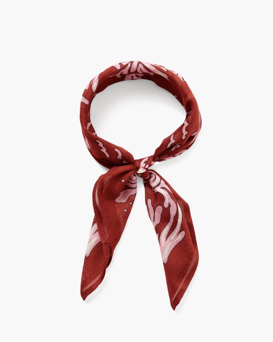 A Seaweed Print Bandana in Red Ochre by Chan Luu tied in a knot, isolated on a white background.