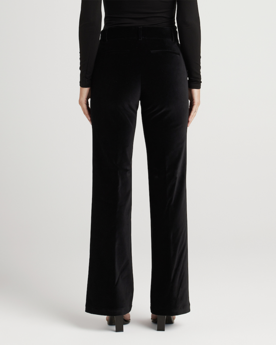 A person standing with their back to the camera, wearing a black velvet flare leg trouser from Edwin and a black top.