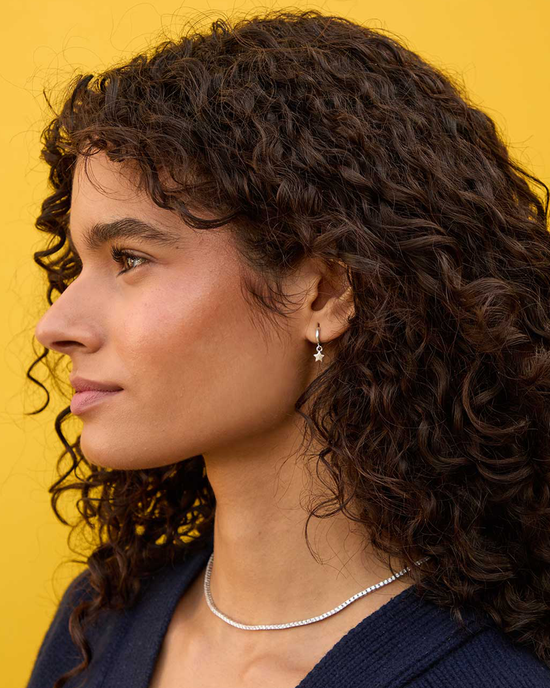 Profile of a woman with curly hair, adorned with Clare V.'s Star Mini Hoops in Sterling Silver, against a yellow background.