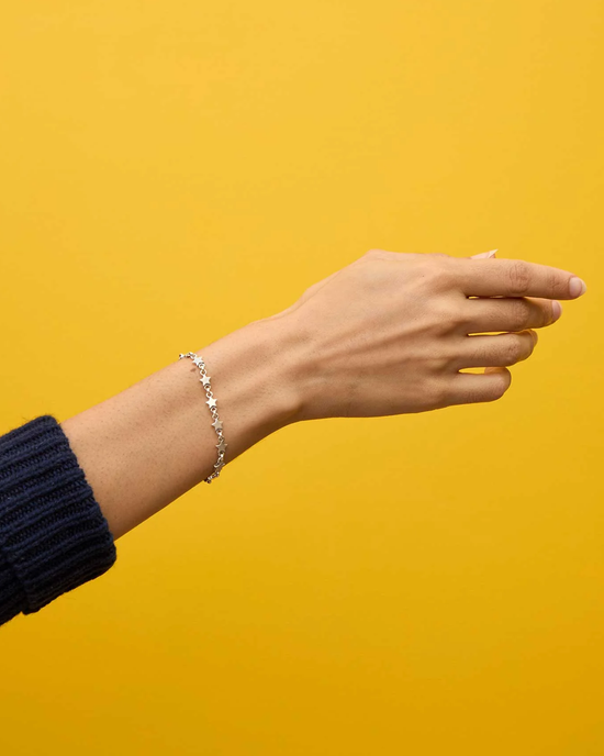 An outstretched hand with a Clare V. Star Strand Bracelet in Sterling Silver against a yellow background.