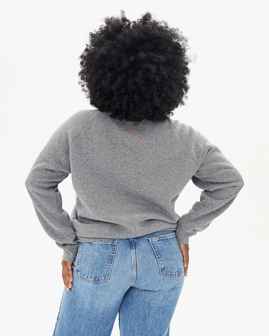 Person with curly hair facing away from the camera wearing a Clare V Oui Sweatshirt in Dark Heather Grey w/ Bright Poppy made in the USA and blue jeans.