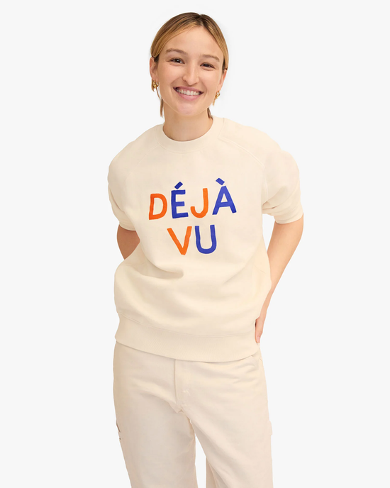 Young woman in a Clare V Flocked Deja Vu Sweatshirt in Cream with Cobalt & Zucca, smiling at the camera. She wears earrings and her hair is pulled back.