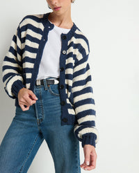 A person stands against a white background, wearing the Nation LTD Tessa Cardigan in Marine Stripe—an oversized, relaxed-fit cotton cardigan—layered over a white tee and blue jeans. The image is cropped at the shoulders and knees.