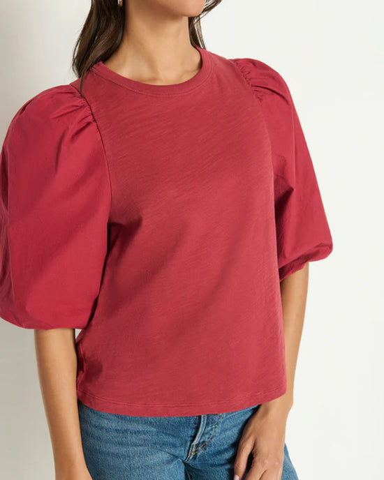 A woman wearing the Nation LTD Tippi Top in Russet with blue jeans stands against a plain light background. Her hair is down, and her face is partly out of frame.