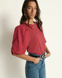 A woman with long brown hair wears the Nation LTD Tippi Top in Russet, styled with high-waisted blue jeans and a black belt. She stands against a plain light background, hands in her pockets.